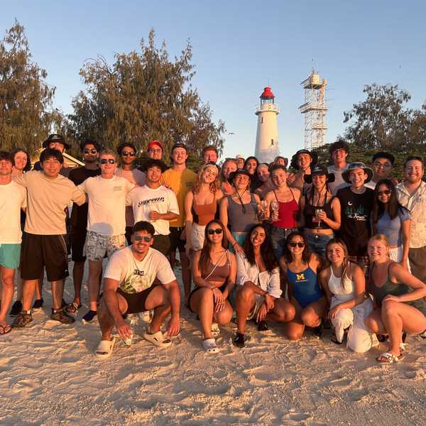 A large group of students posing on a beach. 