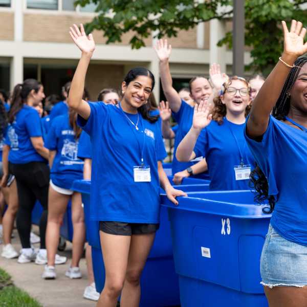 Students wave to incoming students next to blue move-in bins. 