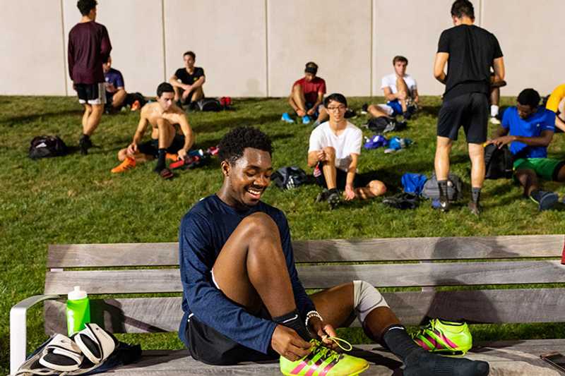 Photo of a group of college-aged athletes sitting in a grassy area getting ready for a match